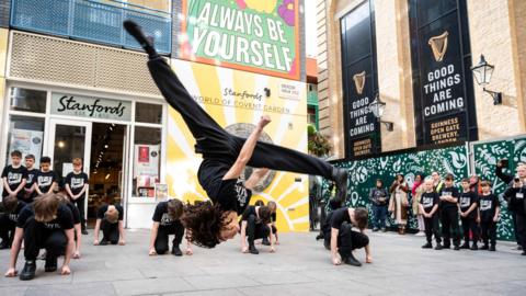 The dancers in action outside in Covent Garden, London. One dancer doing a backflip.