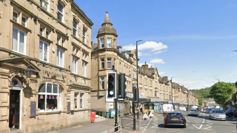 Victorian stone buildings on a busy town street with a pedestrian crossing and cars on the adjacent road.