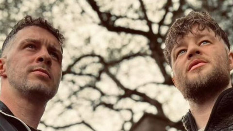 Two men in their mid twenties with beards look off into the distance. 