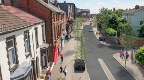 A computer-generated image of how Anfield will look. The image shows people walking along newly paved streets lined with sapling trees, and refurbished houses. Anfield stadium is in the distance. 