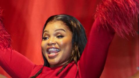 A woman dressed in red stands on stand with her arms in the air.
