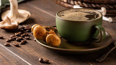 Trendy superfood mushroom coffee in green cup on wooden background. 