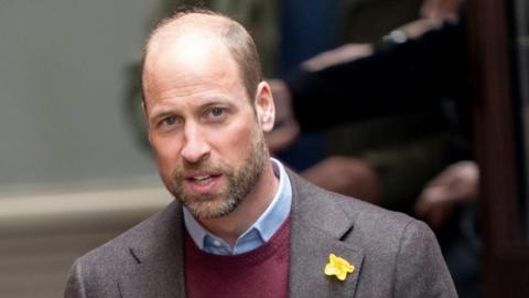 Prince William in a close top shot. He has a daffodil pinned to his suit jacket.
