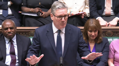 Sir Keir Starmer speaks in the Commons at Prime Minister's Questions. He wears a navy jacket, a white shirt and a navy tie.