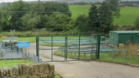 A fenced-off area behind which lie a number of underground tanks.