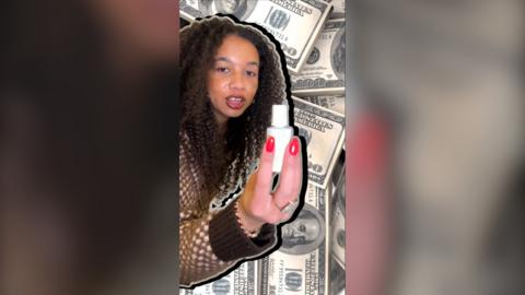 A woman with brown hair wearing a brown cardigan holds up a white bottle of correction fluid against a backdrop of American bank notes.