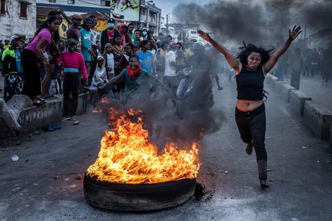 A protester reacts while running past a burning tire used as a barricade during clashes with Malagasy security forces amid a strike calling for constitutional reforms and the resignation of President Andry Rajoelina in Antananarivo, on October 9, 2025