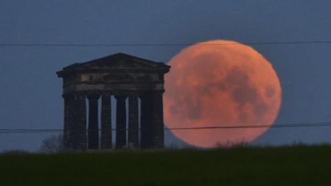 A bright orangey red full Moon, known as the Worm Moon sits to the right of Penshaw Monument, near Sunderland