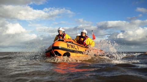 An orange Cleethorpes RNLI lifeboat at sea. There are three crew members wearing yellow jackets and white helmets.