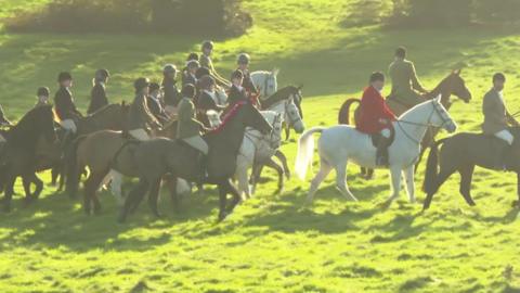 A group of people riding horses through a grassy field. 