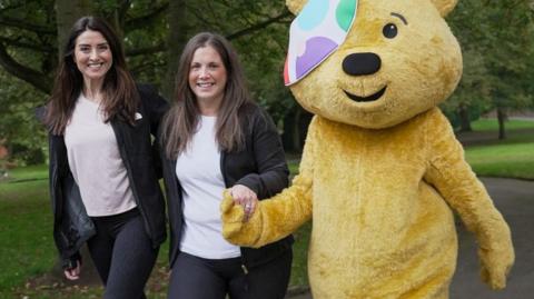 Look North presenter Amy Garcia and Lindsey Burrow walking through a park with Pudsey the bear.