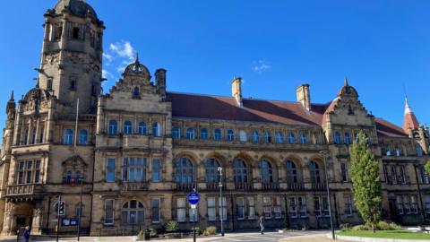 The exterior of Wakefield County Hall has light-brown stone, and is a long building. The sky above is deep blue.