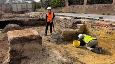 Two people wearing hi-viz and hard hats working in a trench