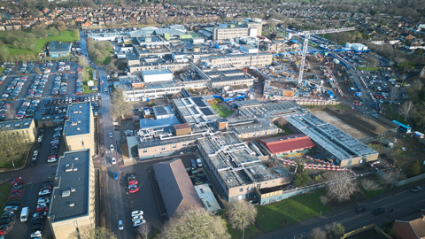 An aerial view of a hospital site with a number of large buildings surrounded by car parks and grassy areas