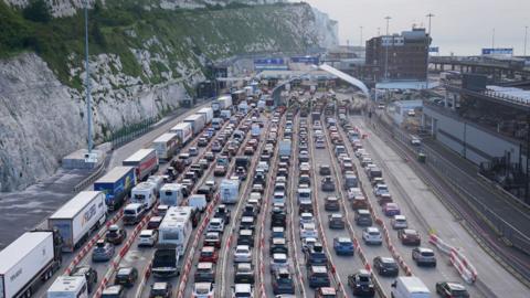 An aerial view over vehicles queuing at the Port of Dover. There are white cliffs on the left and the ocean on the right.