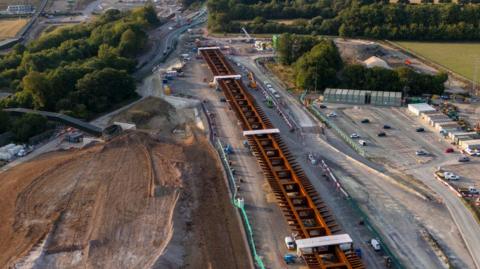 Overhead shot of a HS2 construction site. Pieces of track are being laid with a large brownfield site to the left and a car park to the right