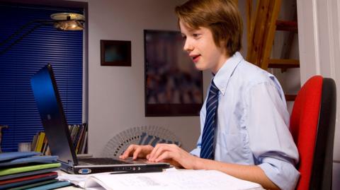 A GCSE student in his bedroom study space with uniform and tie on, using online flashcards to revise.