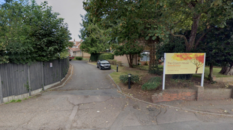 The Coach House in Great Yarmouth. There is a yellow sign on the road with autumnal red and yellow leaves on a tree. 