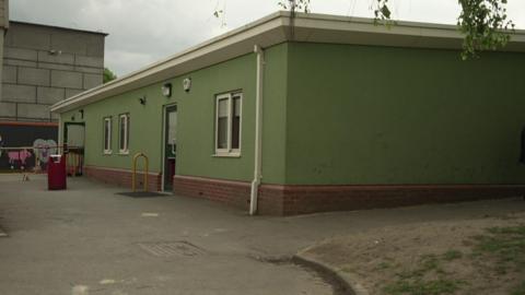 The classrooms are in a green, flat roofed building. 