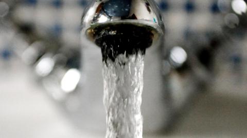 A close up of a silver-coloured tap with clear water pouring out of it.