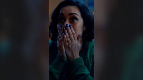 A woman looks surprised and holds her hands over her mouth