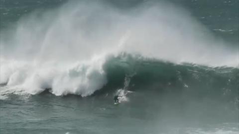 A person on a surfboard. He is surfing a large wave. 