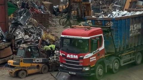 A lorry reversing in a metal recycling firm close to workers who have no barriers to protect them.