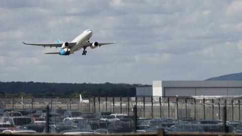 A plane taking off from an airport. There is also a carpark.