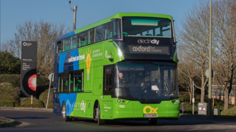 A green electric bus labelled Oxford Bus Company drives out of Oxford Science Park.