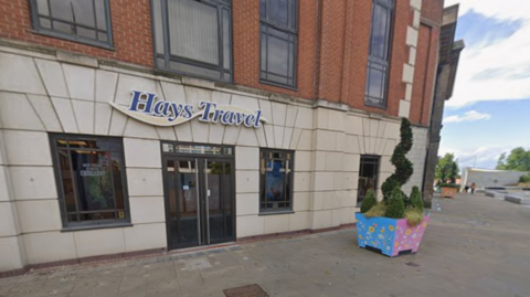 Hays Travel's headquarters on Keel Square in Sunderland. It is within a brown brick building with tall narrow windows. Hays Travel's blue logo with a yellow wave is above the entrance.