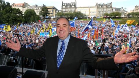 Alex Salmond at a rally for Scottish Independence in Princes Street Gardens, Edinburgh, in 2012. He is smiling at the camera with arms streached out - behind him are thousands of people waving flags and cheering