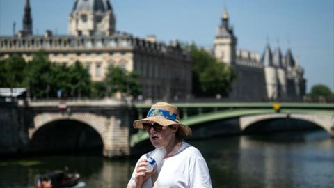 A woman with a hat cools off with a cold bottle of water on the Seine riverside