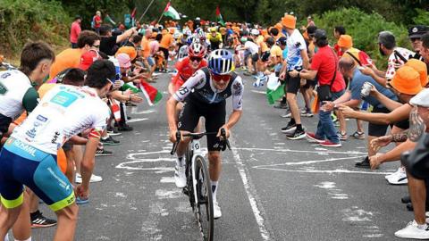 Tom Pidcock riding in the Vuelta a Espana as spectators stand on the road and encourage cyclists