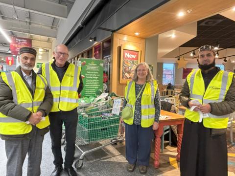 Three men and a a woman wearing hi-vis jackets stand outside a Morrisons supermarket