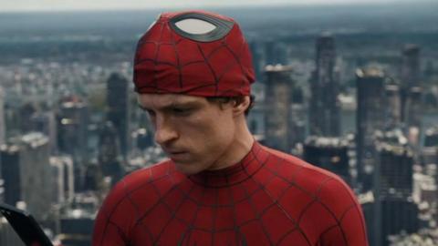 Tom Holland with his Spider-Man mask half off looks at a phone. 