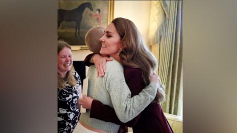 The Princess of Wales hugging Liz Hatton - the princess is wearing a dark red outfit with the side of her head visible. Liz is wearing a green jumper and her head is shaved. 