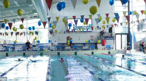 A swimming pool with six people swimming. On the roof are flags and balloons in a celebratory theme.