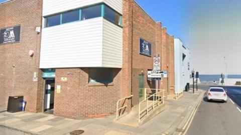 The exterior of the Moore Street public toilets, a red brick building with the seafront at the end of the street.