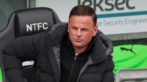 Richie Wellens sitting in the dugout with his right arm bent and hand positioned on his knee