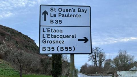 A picture of a road sign directing drivers to La Paulente, a misspelling of La Pulente. The sea, sky and headland are visible in the background.