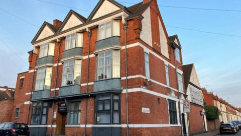 Three storey office block with red brick, white, grey and black windows. A 20 mph sign is to the right of the building.