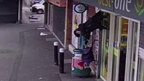 CCTV shows a woman hoisted into the air due to her coat becoming stuck in shop shutters