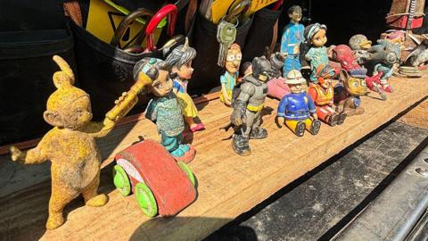 A selection of grubby toys on a wooden shelf, including one of the Teletubbies, Paw Patrol and Disney characters