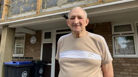 Middle-aged man in t-shirt standing outside the front of his flat on an estate