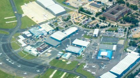 An aerial shot of London Oxford Airport, with a runway, several parked light aircraft and jet aircraft, and hangars