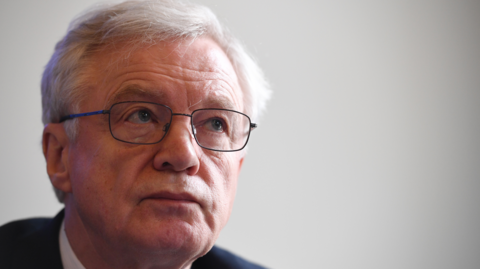 A close up of Sir David Davis. He's wearing glasses and a suit with a white shirt. 