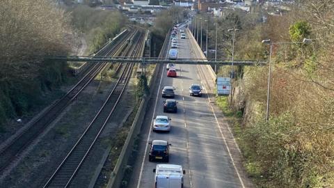 The A48 road pictured from a bridge above, showing cars driving along a road which runs adjacent to a train track.