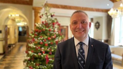 A man wearing a suit and tie in front of a Christmas tree in a hotel foyer