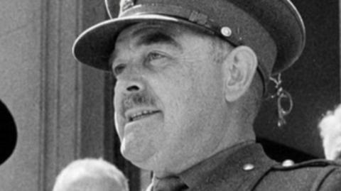 In a black and white image, Brig Snow is standing in full military uniform and looking away from the camera
