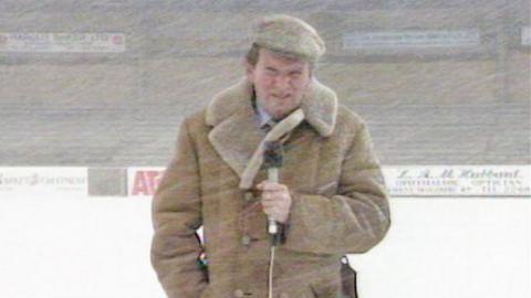 John Motson wears his sheepskin coat during a snow shower
